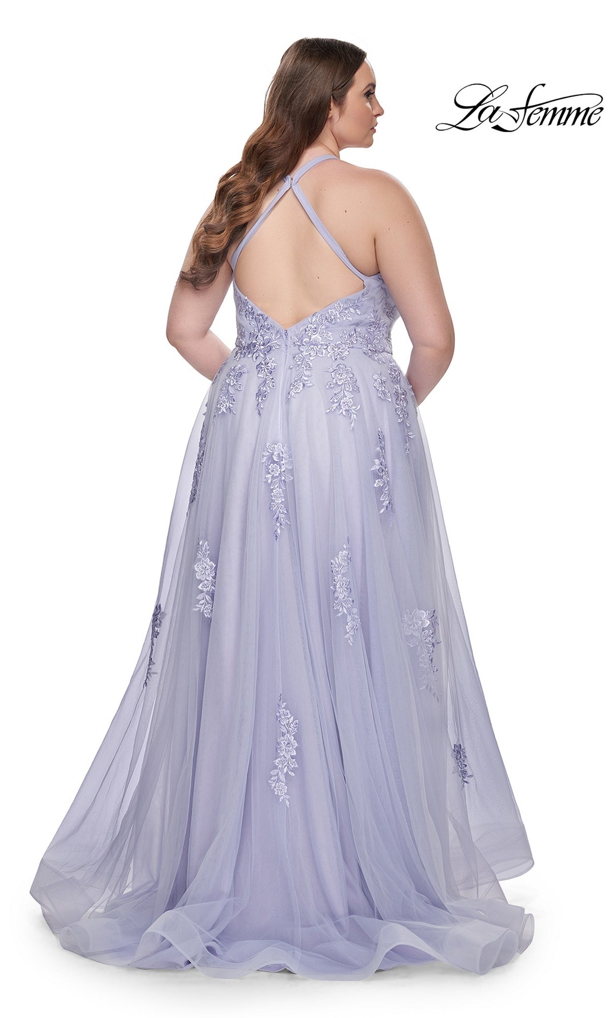 A woman stands facing away from the camera in the La Femme Long Prom Dress 29021, featuring lavender fabric, floral embroidery, and a crisscross back.